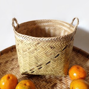 May include: A woven basket with two handles, made of natural materials, sits on a woven tray with three oranges.