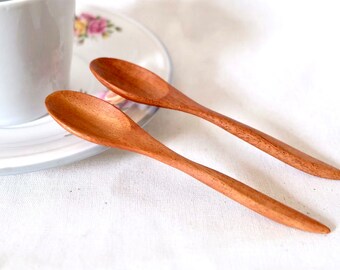 May include: Two wooden spoons with a natural wood finish. The spoons are lying on a white surface.