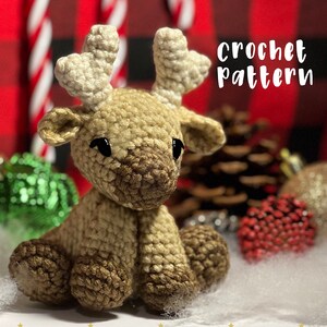 May include: Crochet pattern for a brown and beige amigurumi reindeer with large black eyes. The reindeer is sitting on a white surface with a red and black checked background and candy canes.