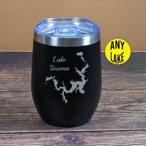 May include: Black stainless steel tumbler with a blue lid. The tumbler has a laser engraved design of Lake Texoma with the words "Lake Texoma" above the design. The tumbler is sitting on a wooden surface.