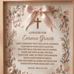May include: A framed wall art piece featuring a light pink satin bow and a small brown cross centered above the text A PRAYER FOR Emma Grace. The prayer text is followed by the date Baptized - March 10, 2026, surrounded by floral embroidery.