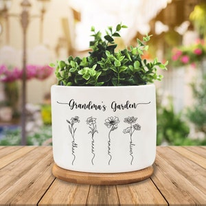 May include: White ceramic planter with a bamboo base. The planter has the text "Grandma's Garden" and four stylised flowers with the names "Ethan", "Anna", "Emma", and "Oliver" written underneath.