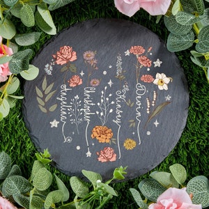 May include: A black slate coaster with a floral design and the names "Devin", "Kinsey", "Christopher", and "Angelina" written in white script.