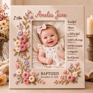 May include: A rectangular photo frame featuring a cream-colored fabric border decorated with embroidered pink, white, and purple flowers. The frame displays the name Amelia Jane, the text I Am, and religious verses. It includes the date November 23, 2026.