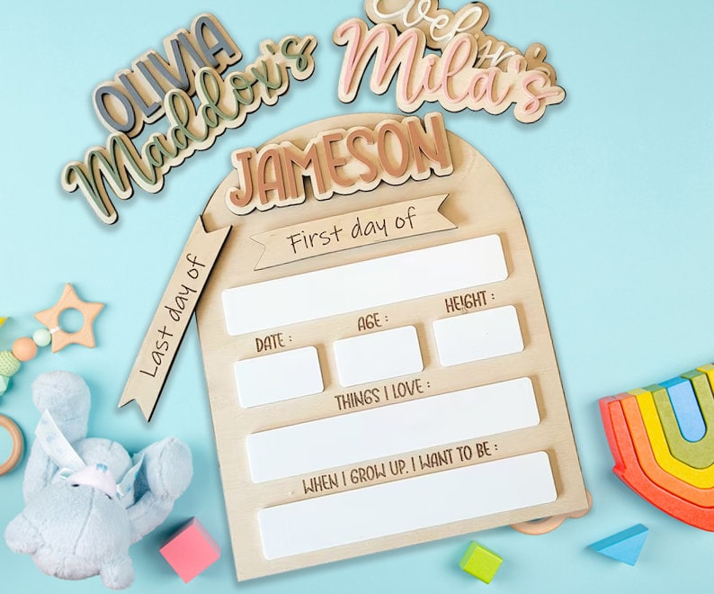 May include: A wooden growth chart with a light brown arch and white spaces to fill in with details about a child's first day and last day. The chart has the text "Last day of" and "First day of" on the left and right sides of the arch. The chart also has the text "Date", "Age", "Height", "Things I Love", and "When I grow up, I want to be".