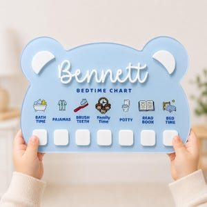 May include: A light blue bear-shaped acrylic bedtime chart featuring the name Bennett in white script. The chart includes seven icons with labels: Bath Time, Pajamas, Brush Teeth, Family Time, Potty, Read Book, and Bed Time, with white squares below.