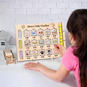 May include: A wooden daily routine board with the text "Olivia's Daily Routine" and various illustrated activity icons. The board includes slots for tasks like brushing teeth, eating breakfast, and outdoor time. Yellow star-shaped reward tokens are included.