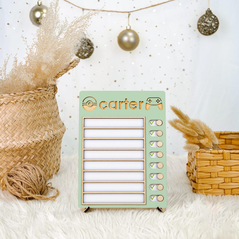 Puede incluir: Un cuadro de tareas de madera verde menta con el nombre "Carter" y un dise&ntilde;o de mando de videojuegos. El cuadro tiene diez l&iacute;neas en blanco para tareas y casillas de verificaci&oacute;n. Elementos decorativos: cesta tejida, plantas secas y adornos.