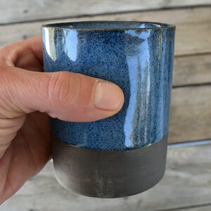 Peut inclure: Une tasse en c&eacute;ramique bleue et brune avec un gla&ccedil;age mouchet&eacute;. La tasse est faite &agrave; la main et a un aspect rustique et artisanal.