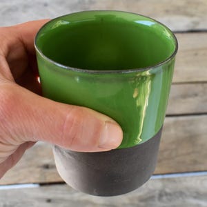 Peut inclure: Une tasse en c&eacute;ramique verte et brune avec un gla&ccedil;age vert brillant. La tasse est tenue dans une main.