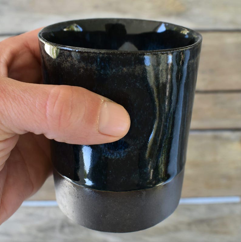 Peut inclure: Une tasse en c&eacute;ramique noire avec un gla&ccedil;age bleu fonc&eacute;. La tasse a une forme l&eacute;g&egrave;rement arrondie et un bord large.