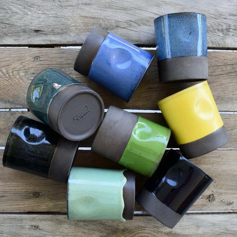 Peut inclure: Un ensemble de huit tasses en c&eacute;ramique de diff&eacute;rentes couleurs, dont le bleu, le vert, le jaune et le noir. Les tasses ont un gla&ccedil;age brun sur la moiti&eacute; inf&eacute;rieure et une vari&eacute;t&eacute; de gla&ccedil;ages sur la moiti&eacute; sup&eacute;rieure. Les tasses sont dispos&eacute;es en cercle sur une surface en bois.