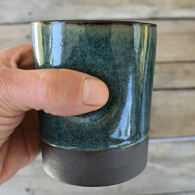 Peut inclure: Une tasse en c&eacute;ramique vert fonc&eacute; avec un bord et une base brun. La tasse a un gla&ccedil;age mouchet&eacute; et une finition brillante.