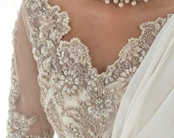 May include: A white bridal saree with intricate beaded embroidery and a pearl necklace. The saree has a sheer, lace-like fabric with a delicate floral pattern.