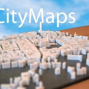 May include: A white 3D printed model of a city with a tall building in the center. The model is on a black surface and the background is a blue sky with white clouds. The text "CityMaps" is visible at the top of the image.