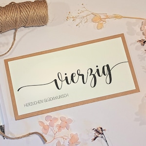 May include: A rectangular greeting card with a cream-colored center and a brown border. The word "Vierzig" is written in black cursive, with "HERZLICHEN GL&Uuml;CKWUNSCH" below it. A spool of twine and dried flowers are in the background.