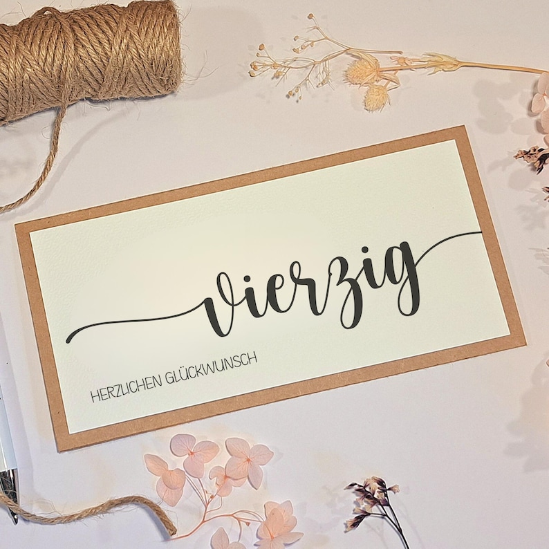 May include: A rectangular greeting card with a cream-colored center and a brown border. The word "Vierzig" is written in black cursive, with "HERZLICHEN GL&Uuml;CKWUNSCH" below it. A spool of twine and dried flowers are in the background.