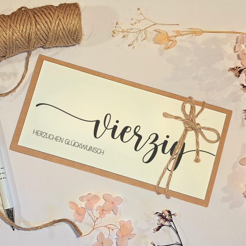 May include: A rectangular card with a cream-colored center and a brown border. The card features the word "Vierzig" in elegant black script, with "HERZLICHEN GL&Uuml;CKWUNSCH" below. A twine bow adorns the right side, with a roll of twine in the upper left.