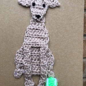 May include: A crocheted brown dog with black eyes and a black nose, holding a green tennis ball.
