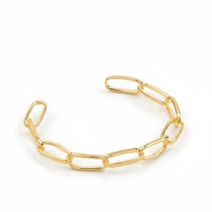 Könnte beinhalten: Ein goldfarbenes Kettengliederarmband mit offenem Manschettendesign. Das Armband hat eine Reihe von länglichen, rechteckigen Gliedern und ist ein modernes Accessoire. Das Armband wird vor weißem Hintergrund präsentiert.