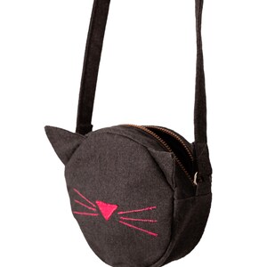 Puede incluir: Un peque&ntilde;o bolso de hombro redondo de fieltro gris con cierre de cremallera y una cara de gato bordada en rosa.
