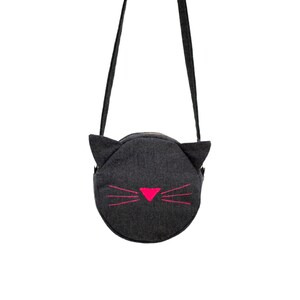Puede incluir: Un bolso bandolera de fieltro gris con una cara de gato negro y bigotes rosas.