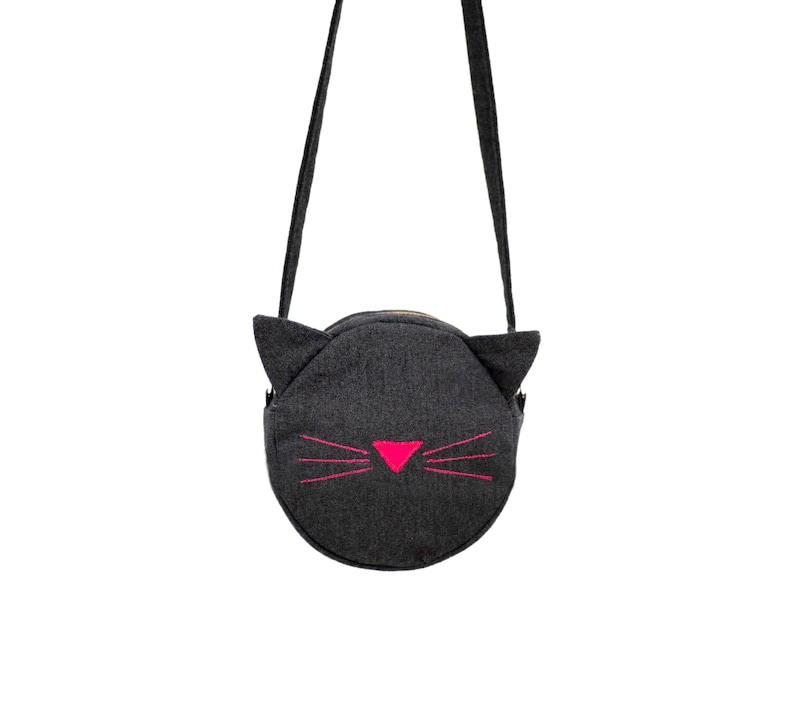 Puede incluir: Un bolso bandolera de fieltro gris con una cara de gato negro y bigotes rosas.