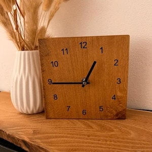 Könnte beinhalten: Eine Holzuhr mit schwarzen Zahlen und Zeigern. Die Uhr steht auf einer Holzoberfläche.