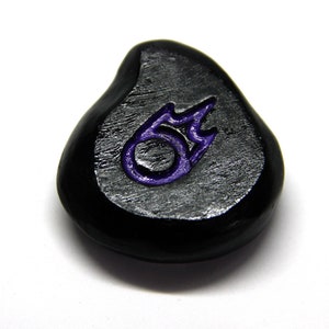 Peut inclure: Une pierre noire en forme de larme avec un symbole de flamme violet gravé.