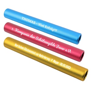 Op de afbeelding: Drie cilindrische estafettestokjes in blauw, rood en goud met een matte afwerking. De blauwe stok is gegraveerd met THOMAS - Viel Erfolg!!!, de rode met 1. Kompanie der Schützengilde Jever e.V. en de gouden met Herzlichen Glückwunsch zur Beförderung - P. Meyer - 28.09.2023.