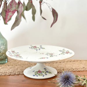 May include: A white ceramic mug with a black handle and the text "But First, Coffee" in a bold, black font. The mug is set against a blurred background, suggesting a cozy setting.