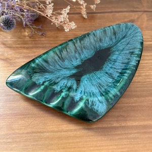 May include: A green and blue ceramic ashtray with a black center. The ashtray is shaped like a triangle with rounded edges.