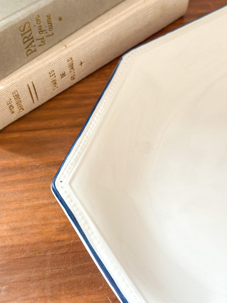 Pu&ograve; includere: Un piatto ottagonale in ceramica bianca con una texture a perline in rilievo lungo il bordo e un sottile bordo dipinto in blu navy. Il piatto presenta una finitura liscia e lucida con un design pulito che mette in risalto la forma geometrica.