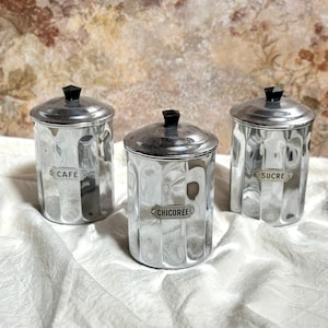 Peut inclure: Trois boîtes en argent avec des couvercles noirs et des étiquettes. Les étiquettes indiquent "Cafe", "Chicoree" et "Sucre".