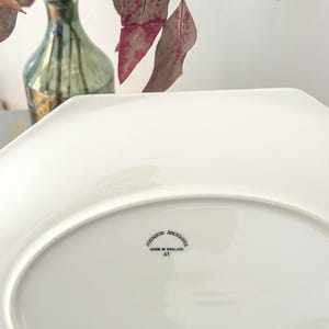Pu&ograve; includere: Un piatto da portata in ceramica bianca con bordo ottagonale. Il lato inferiore presenta un timbro nero con la scritta Johnson Brothers, Made in England, A1. La superficie &egrave; liscia e lucida, mostrando chiaramente il marchio del produttore.