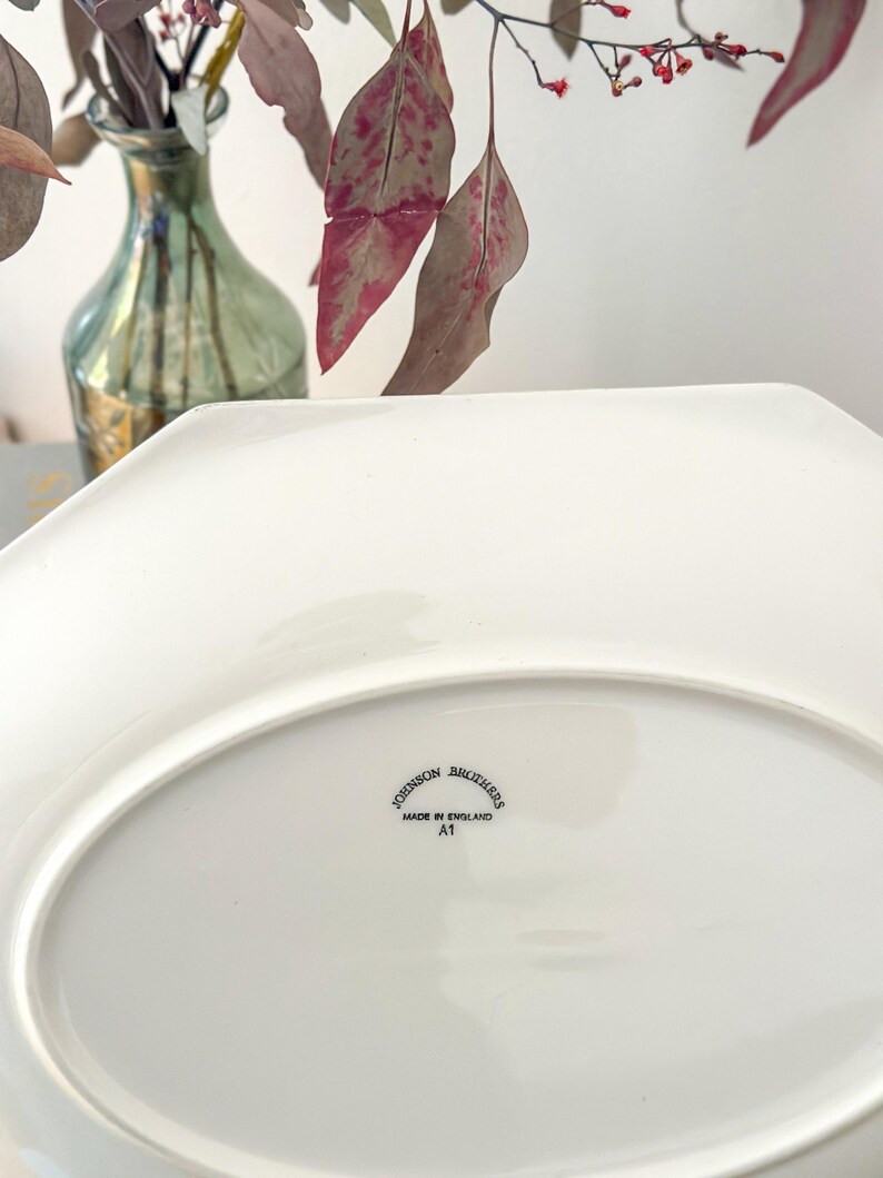 Pu&ograve; includere: Un piatto da portata in ceramica bianca con bordo ottagonale. Il lato inferiore presenta un timbro nero con la scritta Johnson Brothers, Made in England, A1. La superficie &egrave; liscia e lucida, mostrando chiaramente il marchio del produttore.