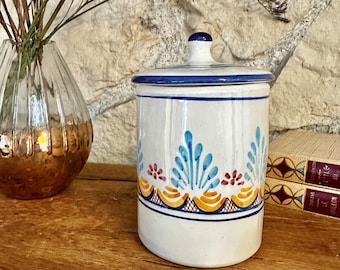 May include: White ceramic jar with a blue and yellow floral design. The jar has a lid and is decorated with blue, yellow, red, and orange accents.