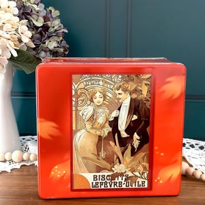 Peut inclure: Boîte en métal rouge avec une illustration vintage d'un couple dans un jardin. Le texte sur la boîte est "Biscuits Lefebvre-Utile".