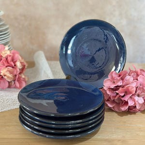 Op de afbeelding: Een stapel van zes blauwe keramische dinerborden met een donkerblauwe rand. De borden zijn gestapeld op een houten oppervlak.
