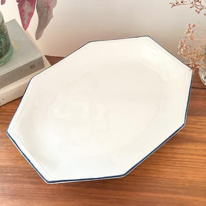 Pu&ograve; includere: Un vassoio da portata ottagonale in ceramica bianca con una finitura liscia e lucida e un bordo sottile blu scuro. Il bordo del vassoio &egrave; dettagliato con una sottile trama a perline in rilievo che segue la forma geometrica del profilo.