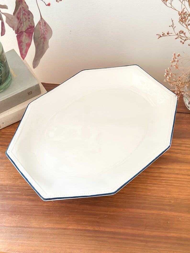 Pu&ograve; includere: Un vassoio da portata ottagonale in ceramica bianca con una finitura liscia e lucida e un bordo sottile blu scuro. Il bordo del vassoio &egrave; dettagliato con una sottile trama a perline in rilievo che segue la forma geometrica del profilo.