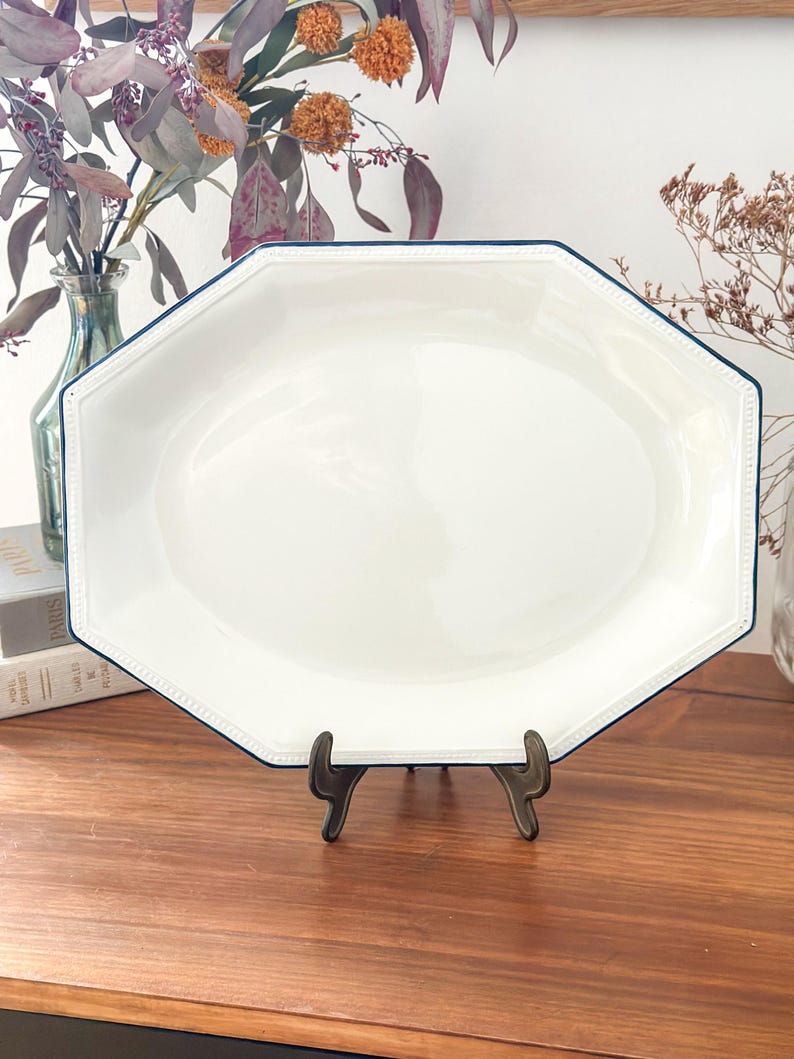 Pu&ograve; includere: Un piatto da portata ottagonale bianco con una finitura liscia e lucida e un bordo sottile blu scuro. Il bordo del piatto presenta un sottile dettaglio in rilievo con texture a perline che corre lungo l'intero perimetro della forma ottagonale.