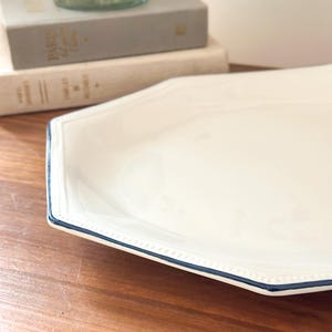 Pu&ograve; includere: Un piatto da portata ottagonale in ceramica bianca con una texture a perline in rilievo lungo il bordo e un sottile bordo dipinto in blu scuro. Il piatto presenta una finitura liscia e lucida e un'ampia superficie piana per servire.