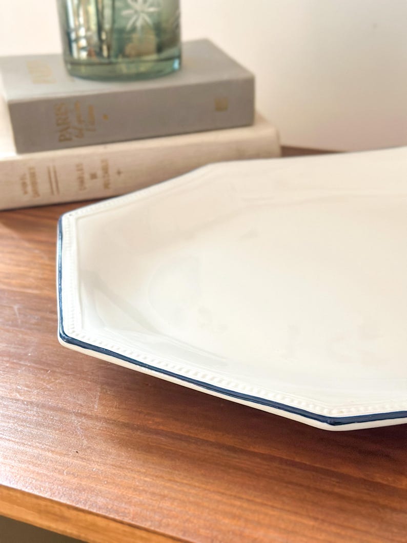 Pu&ograve; includere: Un piatto da portata ottagonale in ceramica bianca con una texture a perline in rilievo lungo il bordo e un sottile bordo dipinto in blu scuro. Il piatto presenta una finitura liscia e lucida e un'ampia superficie piana per servire.