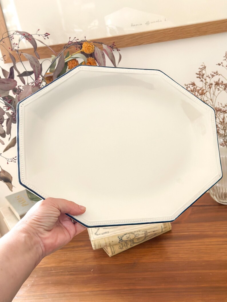 Pu&ograve; includere: Un piatto da portata ottagonale in ceramica bianca con una finitura liscia e lucida e un bordo sottile blu scuro. Il bordo del piatto &egrave; dettagliato con una sottile trama a perline in rilievo che segue la forma geometrica del perimetro.