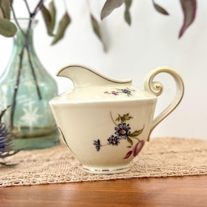 Peut inclure: Crémier en céramique crème avec un motif floral composé de fleurs violettes et bleues et de feuilles vertes. Le crémier a un bec verseur incurvé, une poignée décorative et une bordure dorée. Pièce de style vintage.