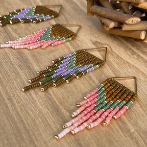 Könnte beinhalten: Vier Paar handgefertigte Perlenohrringe mit geometrischem Design. Jeder Ohrring hat einen goldfarbenen Metallrahmen und farbige Perlen in Rosa-, Grün-, Braun- und Lilatönen. Die Ohrringe haben ein fransenartiges Design.