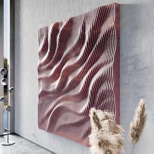 Peut inclure: Une grande œuvre d'art murale carrée en bois avec un motif en forme de vagues. L'œuvre présente des lattes de bois verticales et parallèles dans différentes nuances de rouge et de brun, créant un effet texturé en trois dimensions. L'œuvre est fixée sur un mur gris.