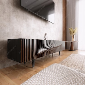 Könnte beinhalten: Ein modernes, dunkelholzfarbenes Entertainment-Center mit einem wellenförmigen, lamellenartigen Design. Das Center hat eine schwarze Oberseite und steht auf vier schwarzen Beinen. Das Center befindet sich vor einer grauen Wand und einem Flachbildfernseher.