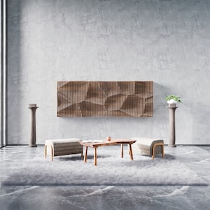 Puede incluir: Una sala de estar minimalista con una pared de hormigón gris, un panel de pared de madera, dos otomanas de color marrón claro, una mesa de café de madera, una alfombra gris y dos columnas de piedra gris con plantas en macetas.